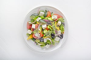 Greek salad of fresh cucumber, tomatoes, bell peppers, lettuce, red onions, feta cheese and olives with olive oil in a white plate