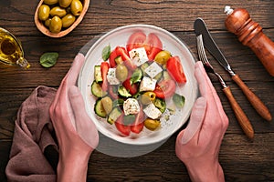 Greek salad. Fresh Greek salad with fresh vegetables, tomato, cucumber, green olives, feta cheese and man hands on old dark wooden