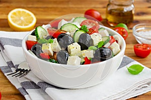 Greek salad of fresh juicy vegetables, feta cheese, herbs and olives in a white bowl on a wooden background. Healthy food.