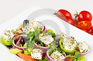 Greek salad with fresh tomato, cucumber, red onion, basil, feta cheese, black olives, Italian herbs and olive oil in white dish on