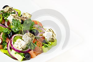 Greek salad with fresh tomato, cucumber, red onion, basil, feta cheese, black olives, Italian herbs and olive oil in white dish on