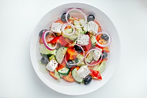 Greek salad with fresh tomato, cucumber, red onion, basil, lettuce, feta cheese, black olives and Italian herbs. Top view