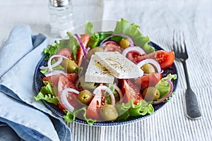 Greek salad of fresh vegetable with tomatoes, lettuce, olives, red onion and feta cheese in bowl