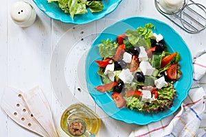 Greek salad with fresh vegetables, feta cheese and black olives in a blue plate on white wooden table.