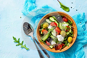 Greek salad with fresh vegetables, feta cheese and black olives on a blue stone or concrete table.