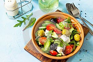 Greek salad with fresh vegetables, feta cheese and black olives on a blue stone or concrete table.