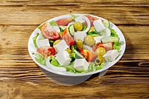 Greek salad with fresh vegetables, feta cheese and green olives on wooden table