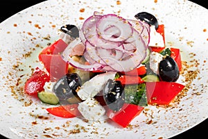 Greek salad with fresh vegetables, olives and feta cheese in plate, isolated on black background. Top view.