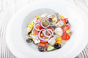 Greek salad with fresh vegetables, olives and feta cheese on wooden background