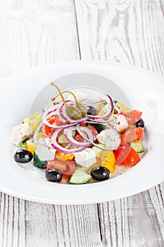 Greek salad with fresh vegetables, olives and feta cheese on wooden background close up. Top view.