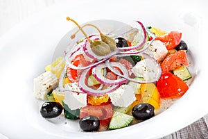 Greek salad with fresh vegetables, olives and feta cheese on wooden background close up.