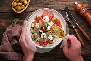 Greek salad. Fresh Greek salad with fresh vegetables, tomato, cucumber, green olives, feta cheese and man hands on old dark wooden