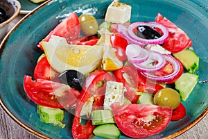 Greek salad of organic vegetables with tomatoes, cucumbers, red onion, olives, feta cheese and glass of wine on wooden background
