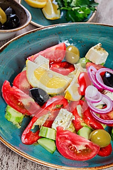 Greek salad of organic vegetables with tomatoes, cucumbers, red onion, olives, feta cheese and glass of wine on wooden background