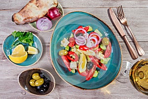 Greek salad of organic vegetables with tomatoes, cucumbers, red onion, olives, feta cheese and glass of wine on wooden