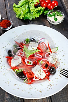 Greek salad of organic vegetables with tomatoes, cucumbers, red onion, olives, feta cheese and sweet pepper on wooden background.