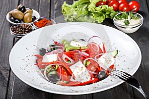 Greek salad of organic vegetables with tomatoes, cucumbers, red onion, olives, feta cheese and sweet pepper on wooden background.