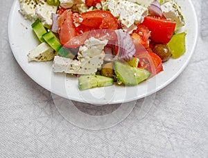 Greek salad plate with original feta cheese, tomatoes, olives, onion and cucumber slices, partial view close up.