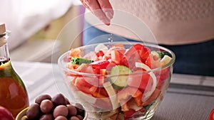 greek salad preparation series concept - woman salting chopped vegetables in a glass bowl