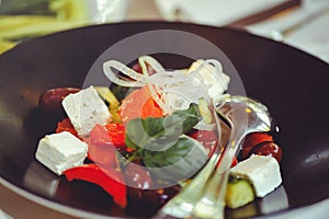 Greek salad with tomatoes, fresh vegetables and cheese in a black bowl close-up. Restaurant serving