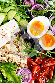 Greek style healthy breakfast bowl with oatmeal porridge and fresh vegetable salad of lettuce, arugula, olives, tomato, cucumber