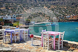 greek tavern with pink and lilac tables and white chairs overlooking Mediterranean sea, Crete, Greece.