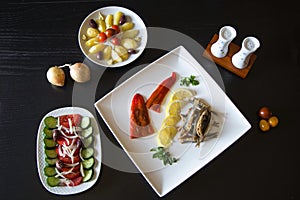 Greek traditional fried anchovies gavros with a sliced lemon on a plate, greek salad and boiled potatoes islolated