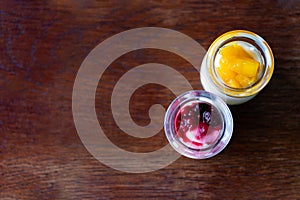 Greek yogurt with berries and mango in glass jars on wooden background