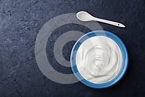 Greek yogurt in blue bowl on black table top view.