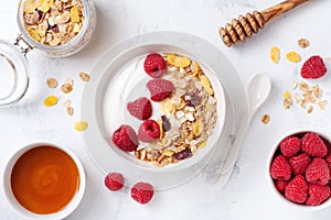 Greek yogurt in bowl with raspberries, honey and muesli on white stone table top view. Healthy diet breakfast