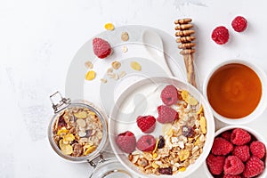 Greek yogurt in bowl with raspberries, honey and muesli on white stone table top view. Healthy diet breakfast
