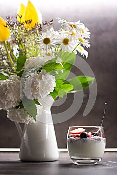 Greek yogurt with coconut chia seeds and fresh fruits next to flowers in the vase