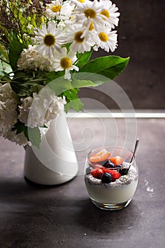 Greek yogurt with coconut chia seeds and fresh fruits next to flowers in the vase