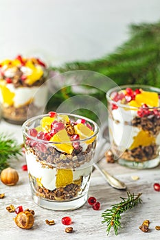 Greek yogurt with granola, orange and pomegranate berries for healthy breakfast on light gray wooden table, copy space