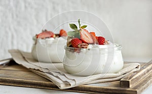 Greek yogurt, nuts and strawberries in a glass jars on a white table close up, copy space