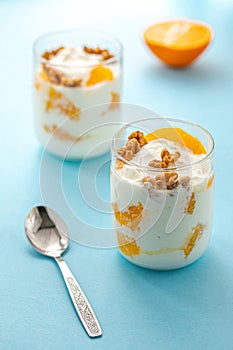 Greek yogurt with orange and walnuts in glasses on a blue table. Healthy food. Health eating concept. Selective focus.