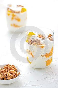 Greek yogurt with orange and walnuts in glasses on a white table. Healthy food. Health eating concept. Selective focus.