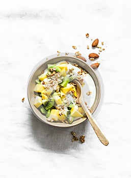 Greek yogurt with tropical fruits kiwi, mango and granola on a light background, top view. Delicious healthy breakfast