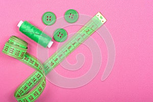 Green accessories for sewing on a pink background.