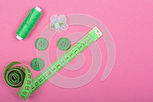 Green accessories for sewing on a pink background.