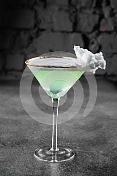 Green alcohol cocktail in a glass decorated with cotton candy on gray background.