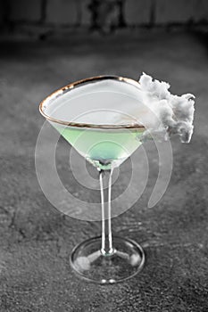 Green alcohol cocktail in a glass decorated with cotton candy on gray background.