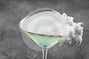 Green alcohol cocktail in a glass decorated with cotton candy on gray background.