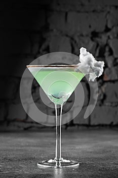 Green alcohol cocktail in a glass decorated with cotton candy on gray background.