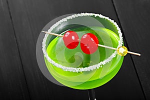 Green alcoholic cocktail with cherry in a glass on dark background.