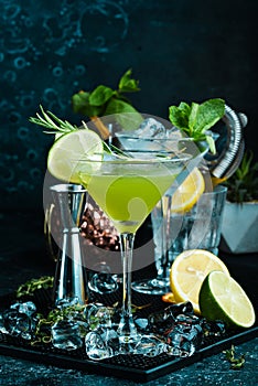 Green alcoholic cocktail with lime and rosemary. On a black stone background. Menu bar
