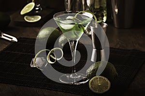 Green alcoholic cocktail monk with dry gin, vermouth, liquor, lime zest and ice, bar tools, dark background