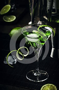 Green alcoholic cocktail monk with dry gin, vermouth, liquor, lime zest and ice, bar tools, dark background