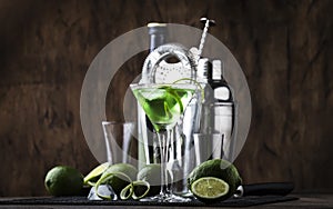 Green alcoholic cocktail monk with dry gin, vermouth, liquor, lime zest and ice, bar tools, dark background