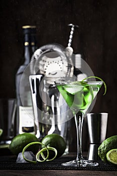 Green alcoholic cocktail monk with dry gin, vermouth, liquor, lime zest and ice, bar tools, dark background